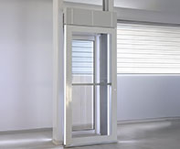 Side view of the LUMA Homelift with the door open, highlighting the glass panels and minimal footprint in a bright room