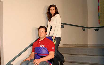 Man wearing red shirt in a Powertrac Power evacuation chair operated by a woman