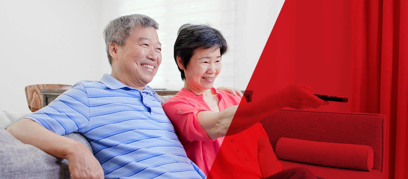 Senior Asian couple sitting on a couch smile while using a remote control