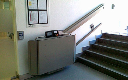 Treppenlift X3 von Garaventa Lift, hier in zugefaltetem Zustand, überwindet das Hindernis Treppe in diesem öffentlichem Gebäude